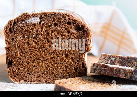 Slices of dark rye bread display a rich texture and deep color on a wooden surface, surrounded by a soft cloth, creating a warm atmosphere. Stock Photo
