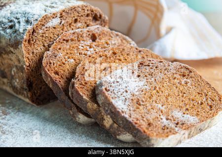 Freshly baked rye bread sits on a wooden surface with slices cut, showcasing its texture and inviting aroma in a warm kitchen atmosphere. Stock Photo