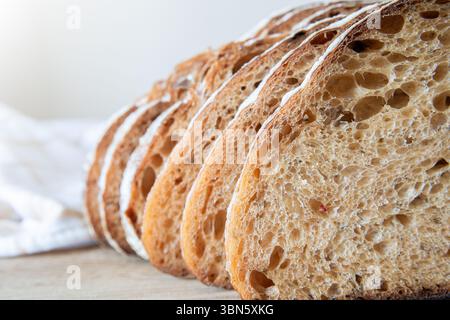 Slices of crusty artisanal bread are laid out on a wooden surface in a bright kitchen, showcasing the texture and color of the loaf. Stock Photo