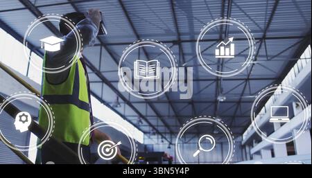 Using tablet worker wearing safety vest by railing monitoring data icons in warehouse, copy space Stock Photo