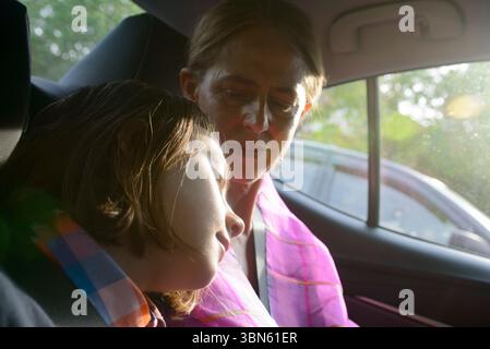 Mother with sleeping son leaning on her shoulder in back seat of car Stock Photo