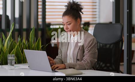 Serious ethnic woman African American girl businesswoman female employer broker agent lady business worker manager look at laptop pc screen work Stock Photo