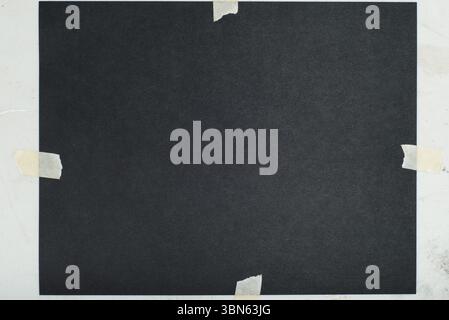 A dark square piece of paper, possibly cardstock, is taped to a lighter background Stock Photo