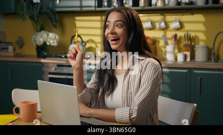 Latina American woman ethnic girl student thinking online studying at home kitchen brainstorm create planning idea solution happy insight female teen Stock Photo