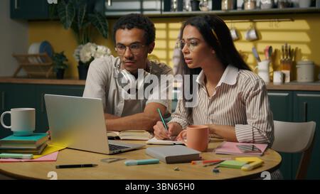 Multiracial woman man studying together at kitchen table high school college students African American guy Latino woman two teenagers use laptop Stock Photo