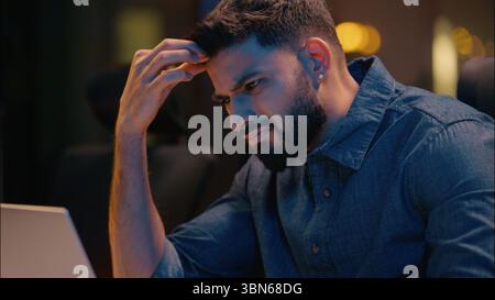 Tired stressed Indian man businessman business employer working laptop overtime evening night office exhausted upset frustrated male worker programmer Stock Photo
