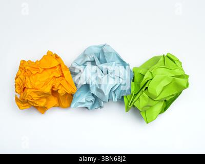 Three crumpled balls of colored paper – orange, light blue, and green – arranged in a row against a white background. Stock Photo