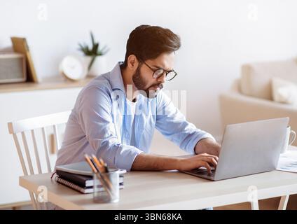 Arab Freelancer Guy Sitting At Desk At Home And Typing On Laptop Stock Photo