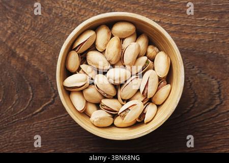 Bowl full of pistachio nuts. Healthy vegetarian snack on wooden table. Natural shelled nuts in rustic dish. Protein-rich food for diet. Stock Photo