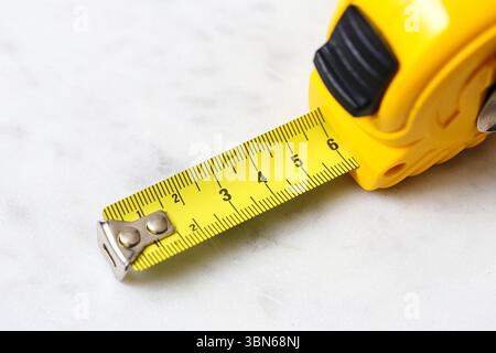 Yellow measuring tape on white background. Tool for home renovation and construction work. Precision in centimeters. Isolated on white marble. Stock Photo