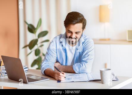 Smiling Arab Man Working With Documents And Laptop At Home Office Stock Photo