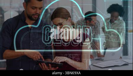 Collaborating professionals reviewing tablet in open-plan office, with laptop papers and cloud icon Stock Photo