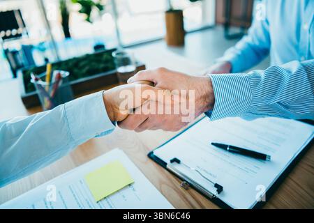 Professional handshake between two individuals confirming agreement in a corporate office setting with documents Stock Photo