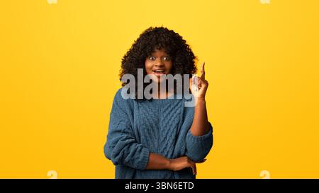 Cute black woman pointing finger up on yellow Stock Photo