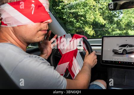 Bavaria, Germany - June 30, 2025: Symbolic image of a self-driving car. Blindfolded and with an unusable steering wheel of a Tesla, the driver stands for the transition to autonomous vehicle control - a symbol of modern driving technology without human intervention. *** Symbolbild Selbstfahrendes Auto. Mit verbundenen Augen und einem nicht nutzbaren Lenkrad eines Teslas steht der Fahrer für den Übergang zur autonomen Fahrzeugsteuerung ein Sinnbild moderner Fahrtechnologie ohne menschliches Eingreifen. Stock Photo