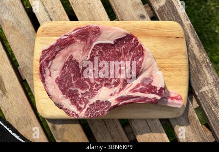 raw bio steak with bone on wooden table background, top view, selective focus, outdoors Stock Photo