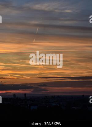 Dramatic evening sunset with illuminated clouds and warm color transitions, silhouetted cityscape enhancing the glowing sky above Stock Photo