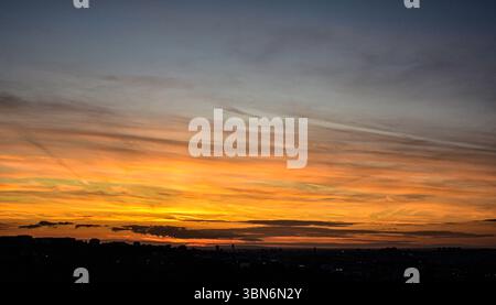 Glowing sky at sunset featuring colorful gradients and soft clouds with city skyline in dark silhouette at the bottom Stock Photo