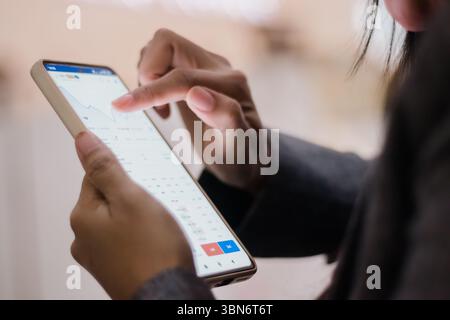 Woman analyzing market data on her smartphone. She's navigating stock trends with an intuitive mobile trading app for insightful investment choices. Stock Photo