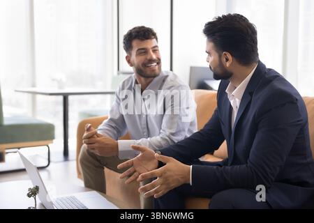 Smiling young businessman talk to male colleague sitting on couch Stock Photo