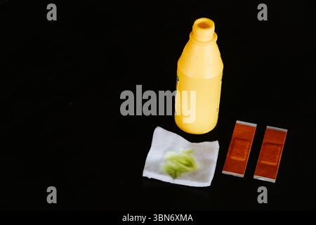 First aid kit supplies, including a yellow antiseptic bottle, bandages, and tissue used to clean a wound, arranged on a black background. Stock Photo
