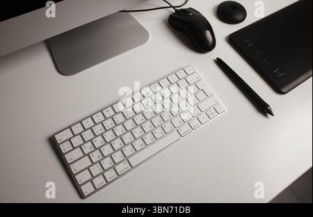 Minimalist home office workspace with a desktop computer, keyboard, notebook, pen tablet on a clean white desk. Freelance at home. Art at home. Stock Photo
