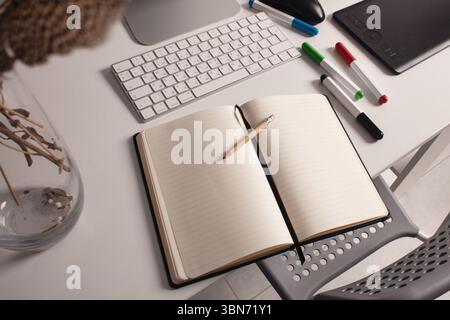 Modern workspace with keyboard, black notebook, pencil, graphic tablet, and pens on white desk. Top view for creative project. Stock Photo