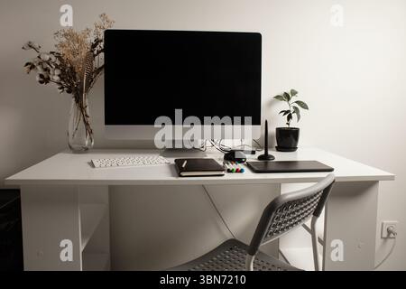 Minimalist home office workspace with a desktop computer, keyboard, notebook, pen tablet, dried flowers and a plant on a clean white desk.Work at home Stock Photo