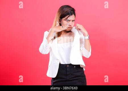 A woman in a white jacket and black pants is adjusting her jacket and posing in front of the camera, isolated on a red background Stock Photo