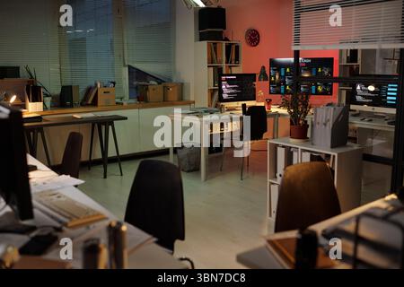 Empty office with multiple computer workstations displaying scam call center dashboards, monitors showing fraudulent activity screens, desks arranged for telemarketing operations Stock Photo