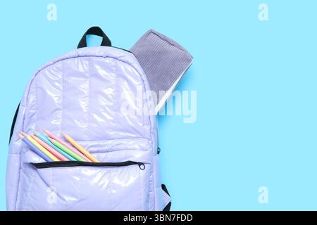 Lilac school backpack with stationery on blue background Stock Photo