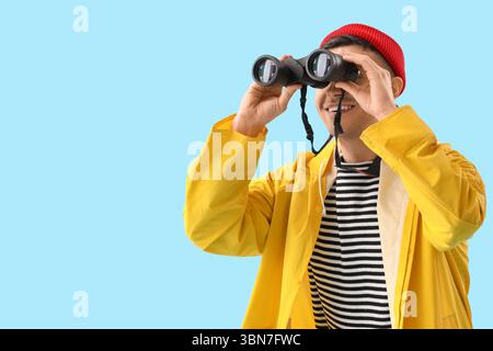Young sailor looking through binoculars on blue background Stock Photo