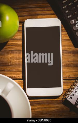White smartphone is lying on tabletop in flat design, showing blank black screen, cup and notebook Stock Photo