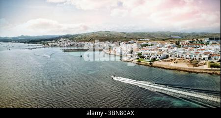Speedboat is cutting through bay water in flat design with white red roofed houses, moored boats Stock Photo