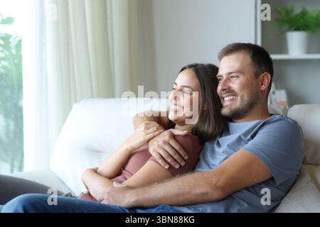 Happy couple hugging and relaxing sitting in a couch at home Stock Photo