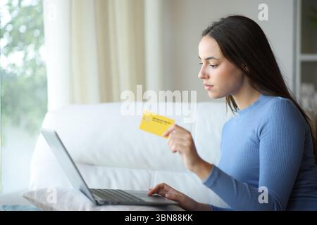 Serious woman using credit card to pay online with laptop sitting on a couch at home Stock Photo