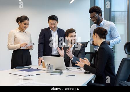 Diverse business team celebrates a success in a modern office setting. Colleagues are gathered around a table, applauding and collaborating. Stock Photo