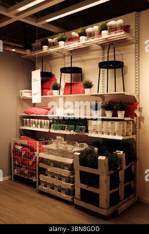 IKEA shelf unit filled with vibrant red pillows, artificial plants, glass containers, and kitchen accessories arranged in a clean, organized display. Stock Photo