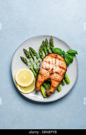 Grilled salmon fish steak over roasted asparagus on blue background, top view, copy space. Balanced keto lunch, healthy eating concept mockup. Stock Photo