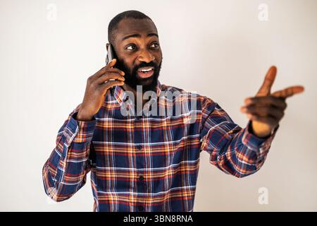 Cheerful black man in cozy shirt standing in front of wall and talking on mobile phone. Stock Photo