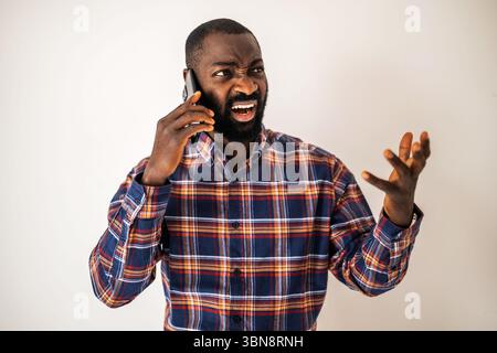 Angry black man in cozy shirt standing in front of wall and talking on mobile phone. Stock Photo
