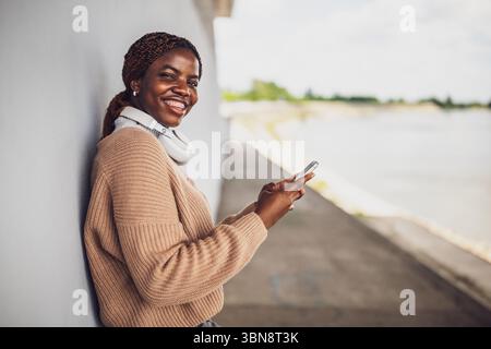 Portrait of young black woman who is messaging on smartphone. Stock Photo