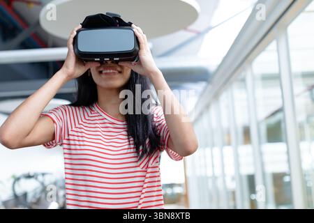 Woman adjusting virtual reality headset in tech office with circular light and glass partitions Stock Photo