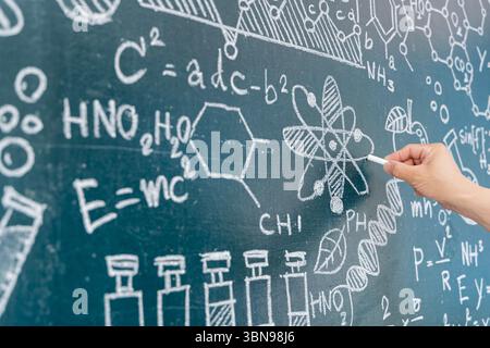 Close-up of hand writing chemical formulas and atomic structure using chalk on blackboard. Represents science education, chemistry class, research, an Stock Photo