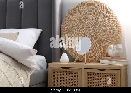 Bedside table with mirror, decor and books near bed indoors Stock Photo