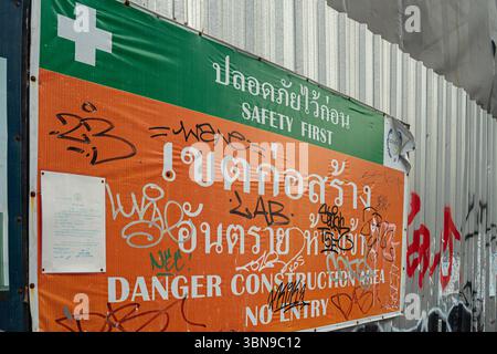 Safety first sign and construction site sign in Thai and English is covered with graffiti. Bangkok, Thailand Stock Photo
