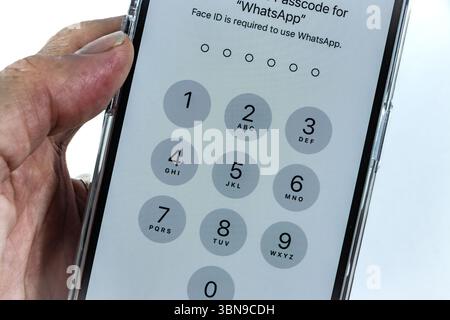 Close-up of a person holding a smartphone displaying a numeric keypad for WhatsApp passcode entry with Face ID requirement on iPhone 14 Pro Stock Photo