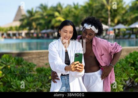 Trendy digital creator couple taking selfie by the beach, sharing travel content for social media Stock Photo