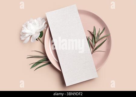 Blank 4x9 menu card with plate, peony flower and eucaliptus leaves on neutral beige background. Minimal elegant wedding invitation card mockup with fl Stock Photo