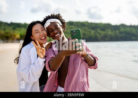 Trendy digital creator couple taking selfie by the beach, sharing travel content for social media Stock Photo